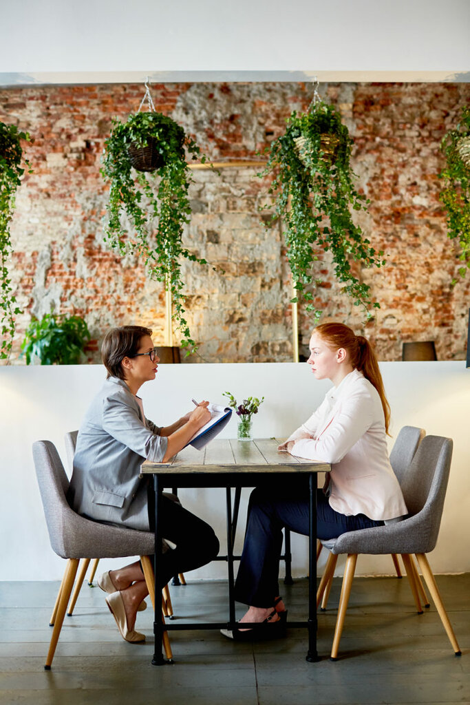 Side view of employer with document and young applicant looking for job in cafe