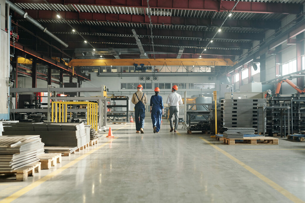 Rear view of three technicians or engineers of industrial plant in workwear leaving workshop at the end of working day