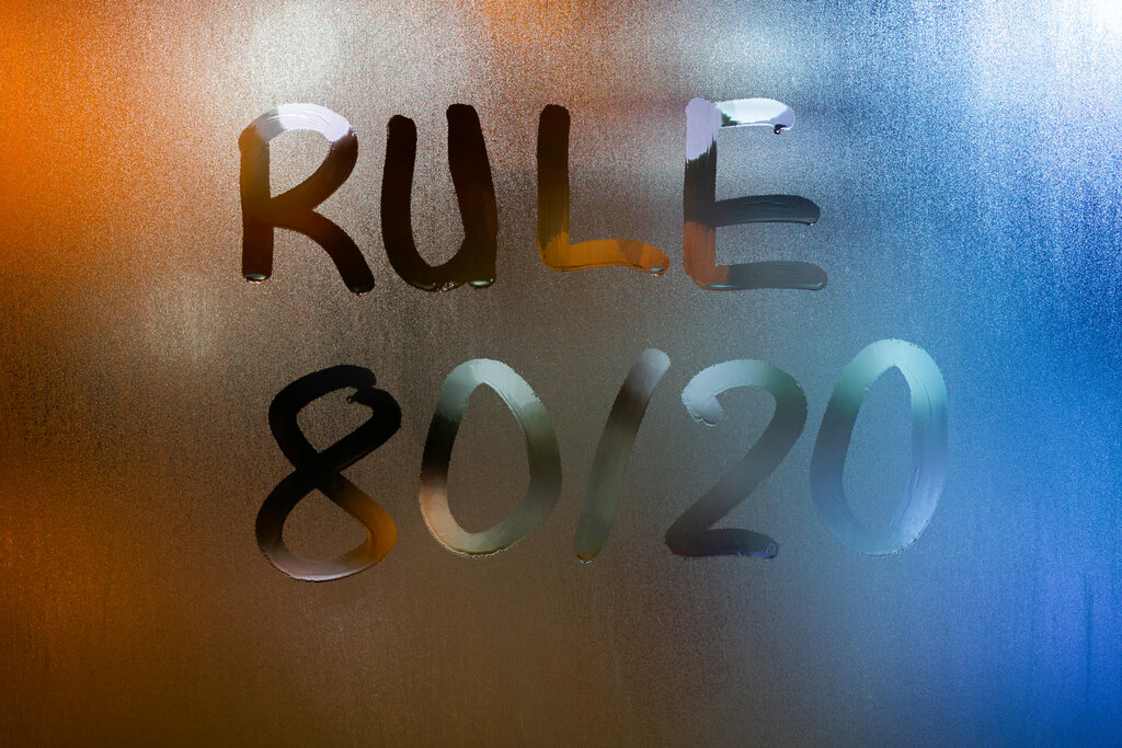 the phrase rule 80 by 20 – pareto principle – handwritten on classic blue night wet window glass with selective focus and blur